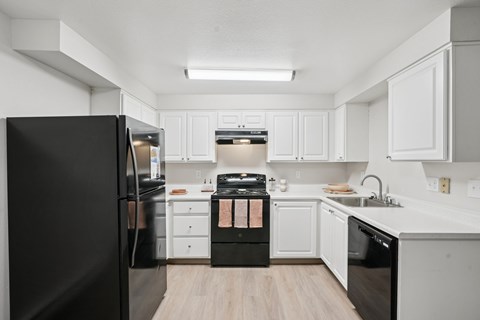 A black refrigerator is in a kitchen with white cabinets.