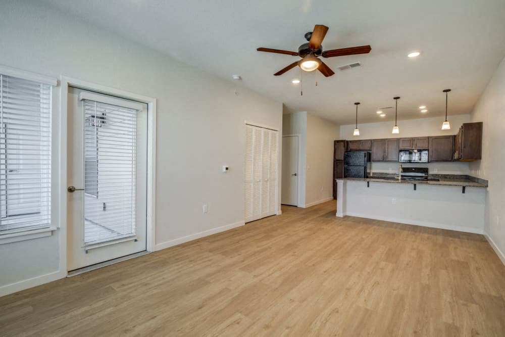 an empty living room with a kitchen and a ceiling fan