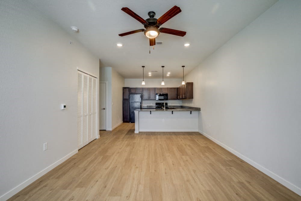 an empty living room with a ceiling fan and a kitchen