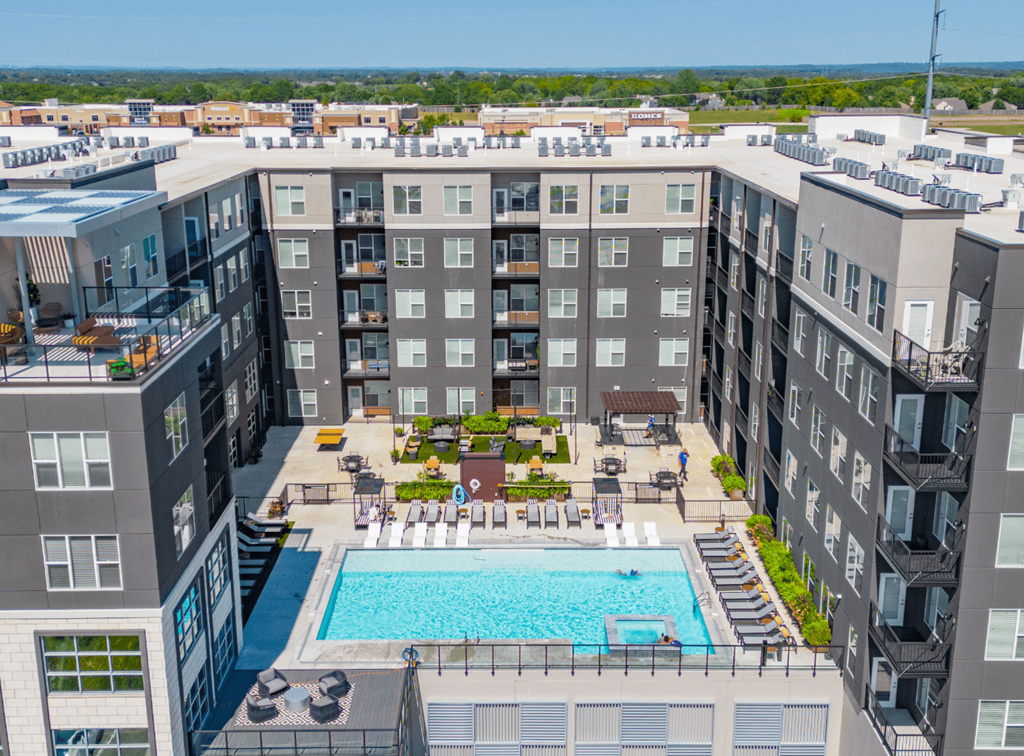 A large swimming pool is surrounded by lounge chairs in the middle of a courtyard.