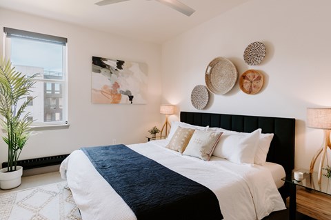 A bedroom with a large bed and a plant at Vina Apartments in Denver, CO.
