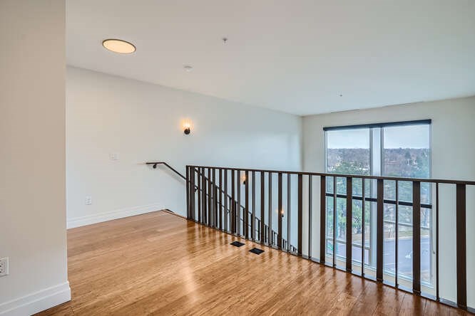 A room with a wooden floor and a balcony with a black railing.
