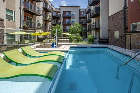 A swimming pool with yellow sun shades in front of apartment buildings.