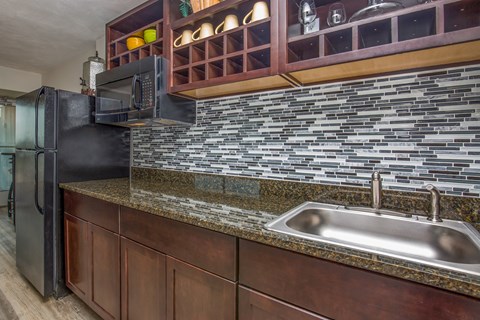 A kitchen with a black refrigerator and a granite countertop.