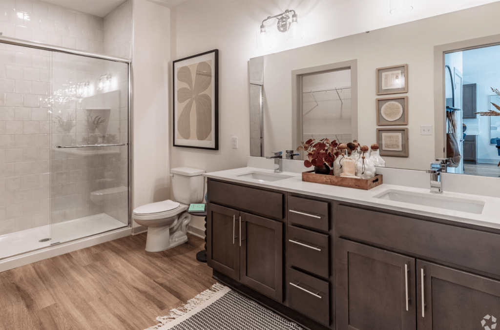 A bathroom with a walk-in shower, toilet, and double sinks.