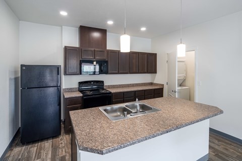 A kitchen with a black refrigerator, brown cabinets, and a granite countertop.