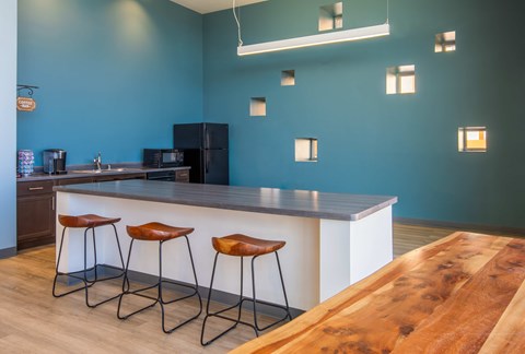A kitchen with a bar area and three stools in clubhouse