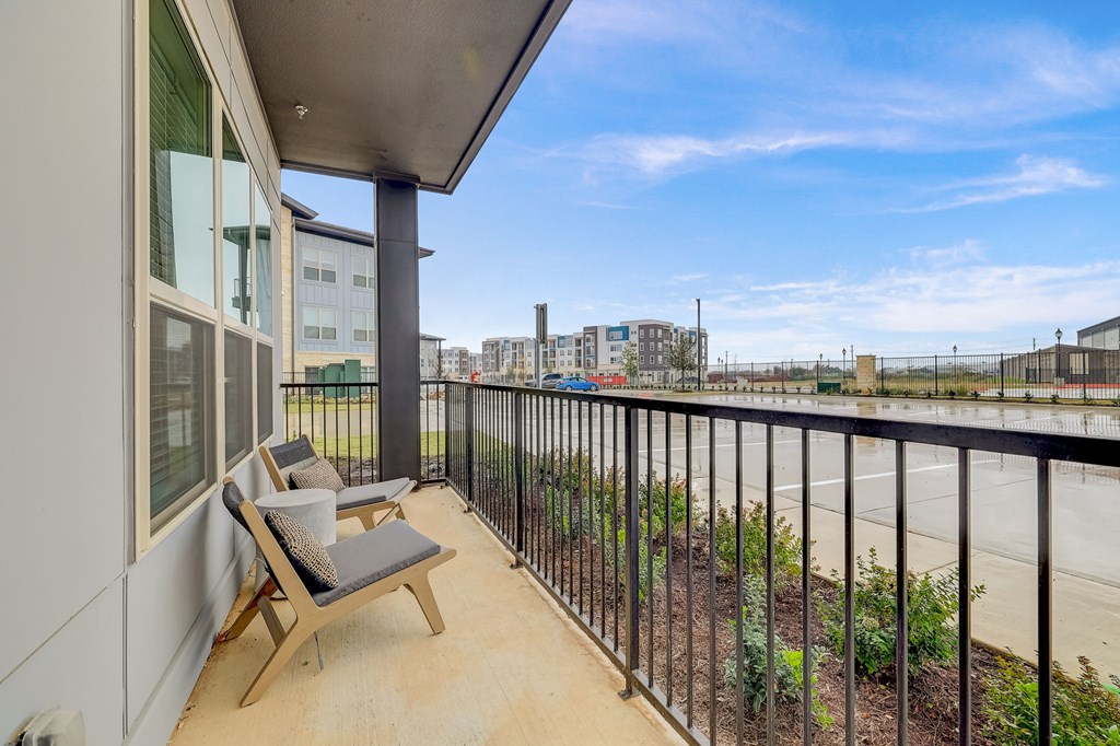 A balcony with a chair and table overlooking a city street.