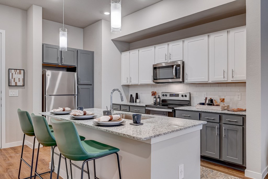 A kitchen with a table set for two and green chairs.