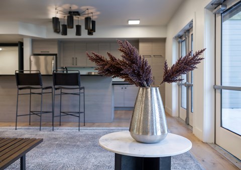 A silver vase with purple plants sits on a white table in a modern kitchen.