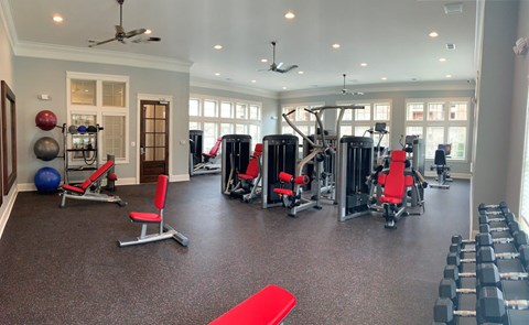 A spacious gym with a variety of equipment including weights, machines, and a red mat.