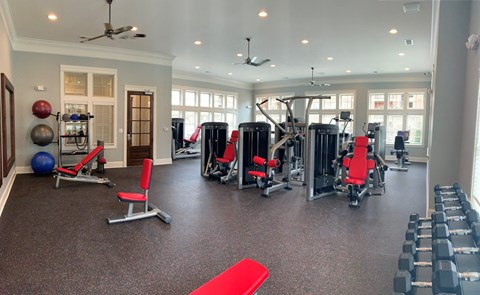 A spacious gym with a variety of equipment including weights, machines, and a red mat.