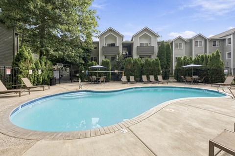 A swimming pool surrounded by a concrete patio and lounge chairs.