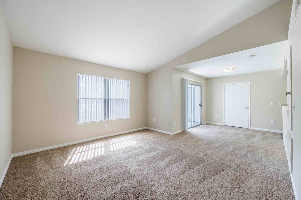 A spacious room with a carpeted floor and a window with blinds.