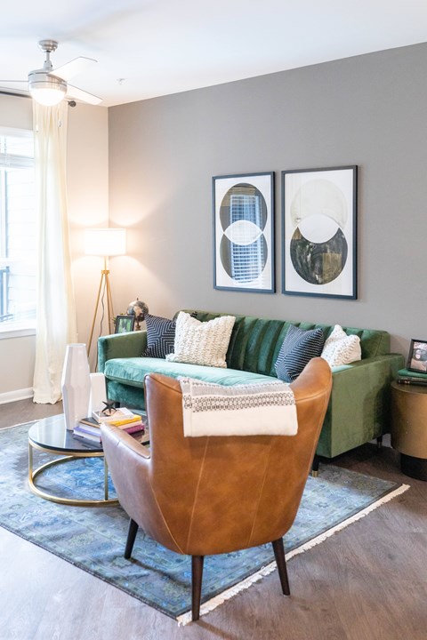 A living room with a green couch, a brown chair, and two framed pictures on the wall.
