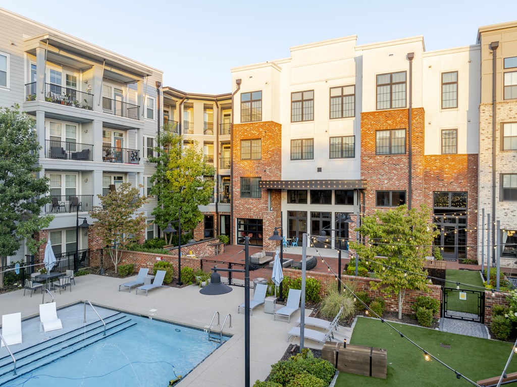 A swimming pool is surrounded by lounge chairs in a courtyard.