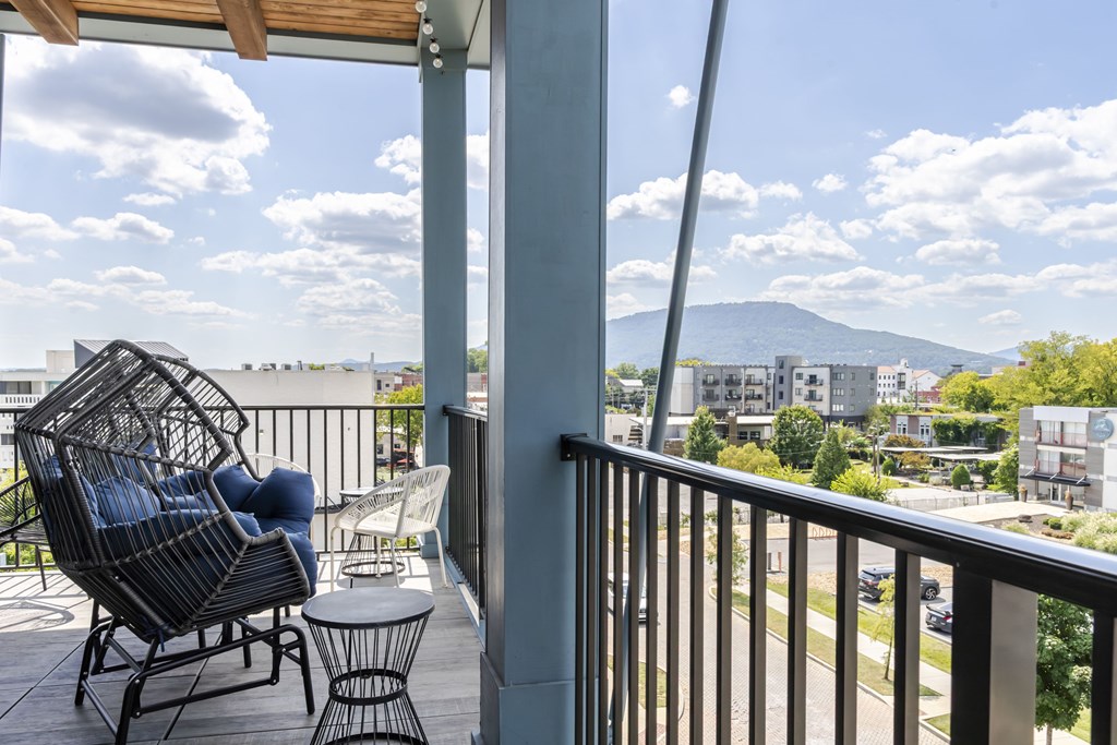 A balcony with a chair and table overlooking a cityscape.