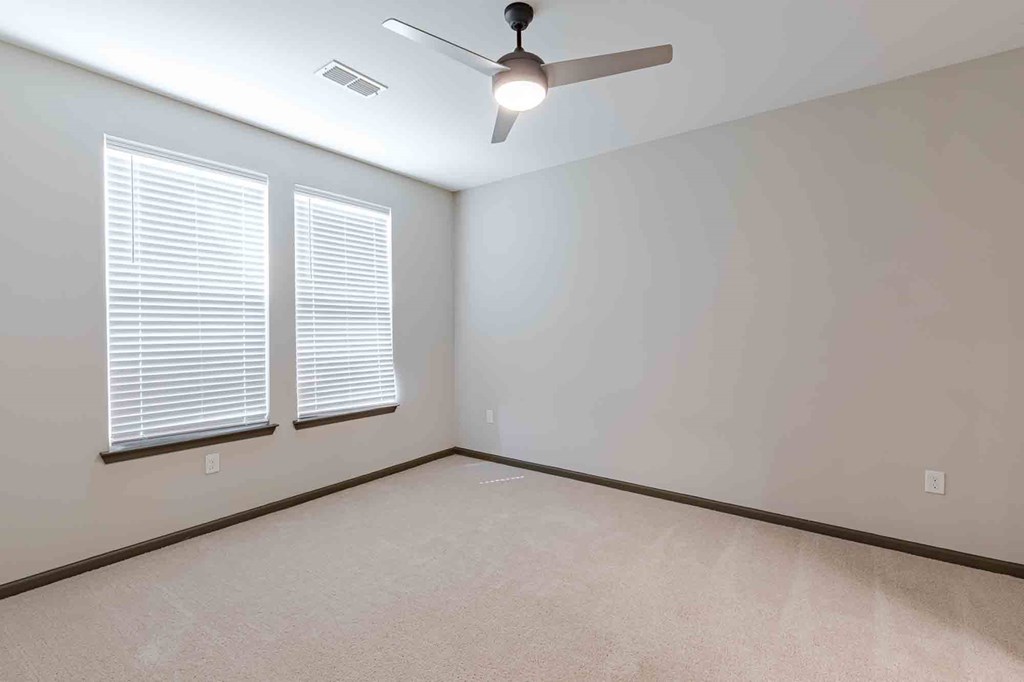 A room with a ceiling fan and two windows.