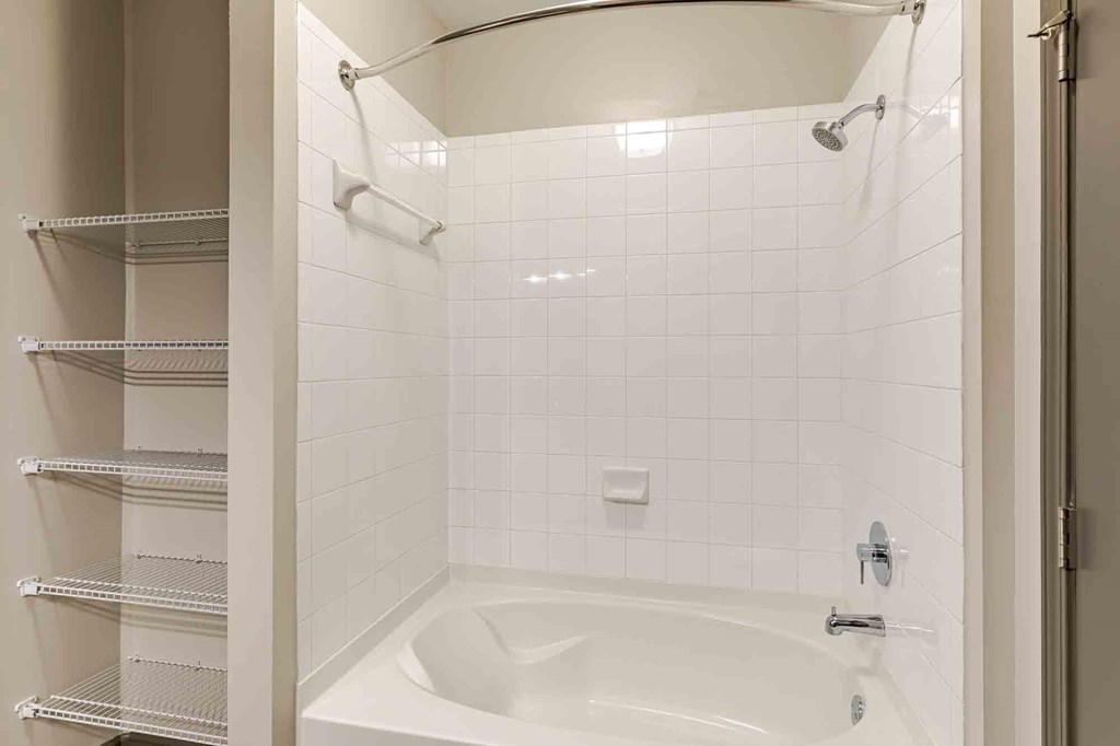 A white tiled shower with a white tub and a white shower head.
