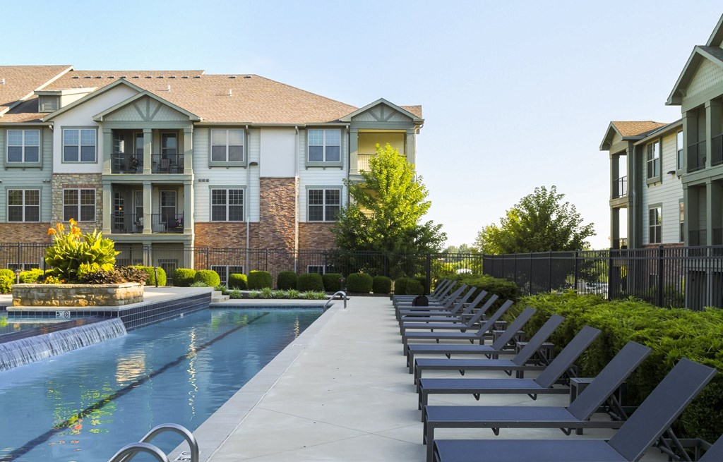 A swimming pool with lounge chairs is in front of a building.