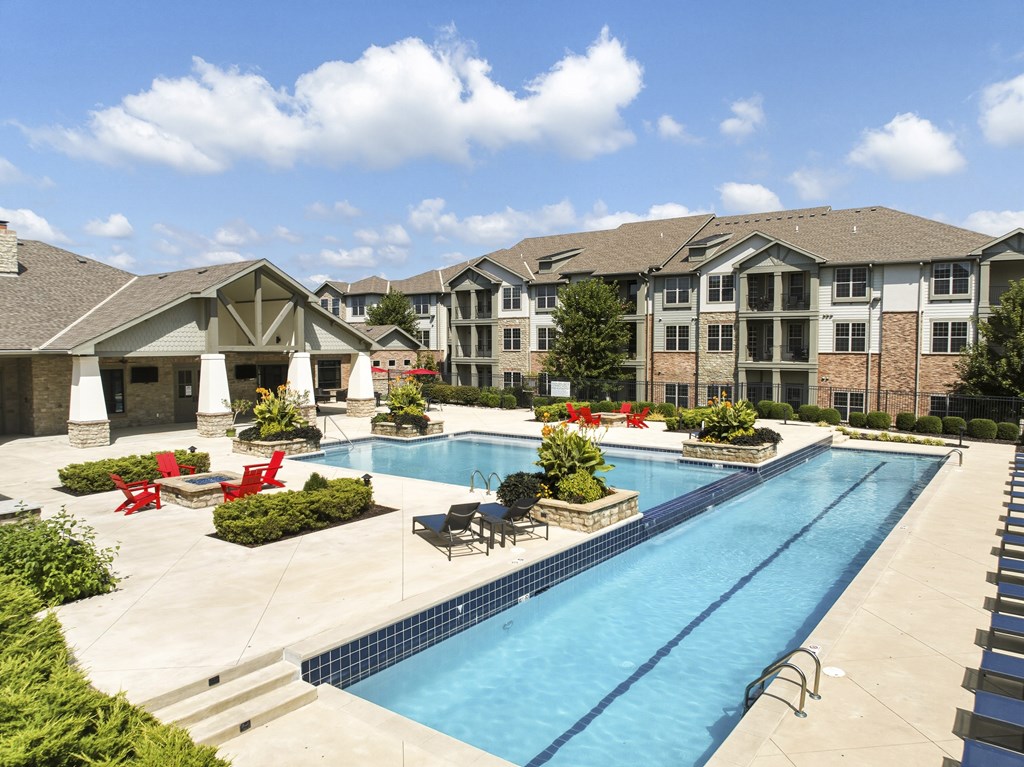 A large swimming pool surrounded by red chairs and plants.