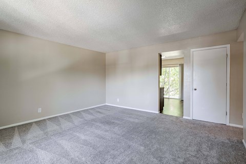 an empty living room with carpet and a door to a hallway