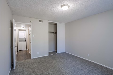 an empty living room with a closet and a hallway to a kitchen