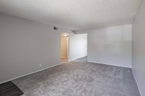 the living room and dining room of an apartment with carpeting and white walls