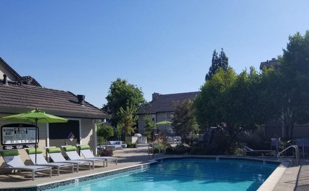 a swimming pool with chairs and umbrellas next to a house