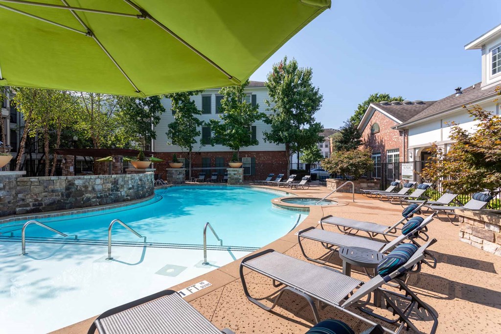 A pool with sun loungers and a green umbrella.