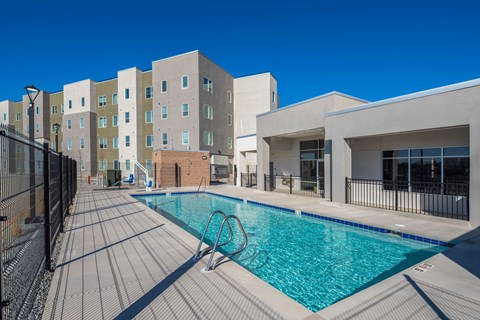 A swimming pool surrounded by a black fence and a building in the background.