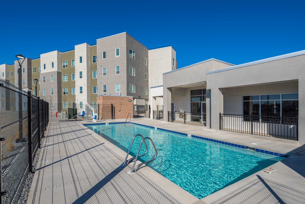 A swimming pool surrounded by a black fence and a building in the background.