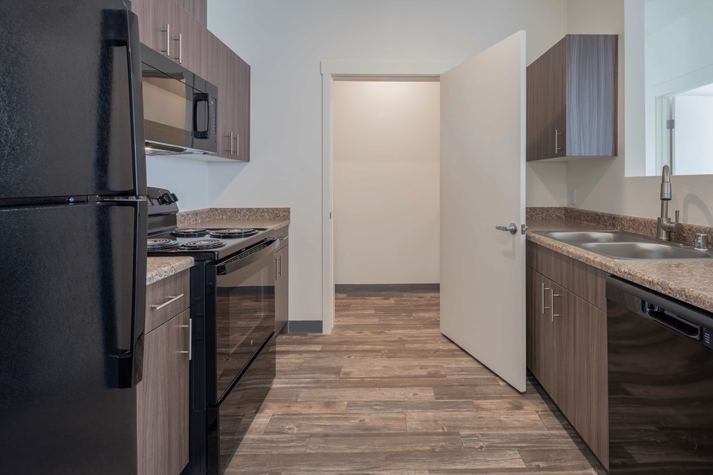 A kitchen with a black refrigerator and wooden flooring.