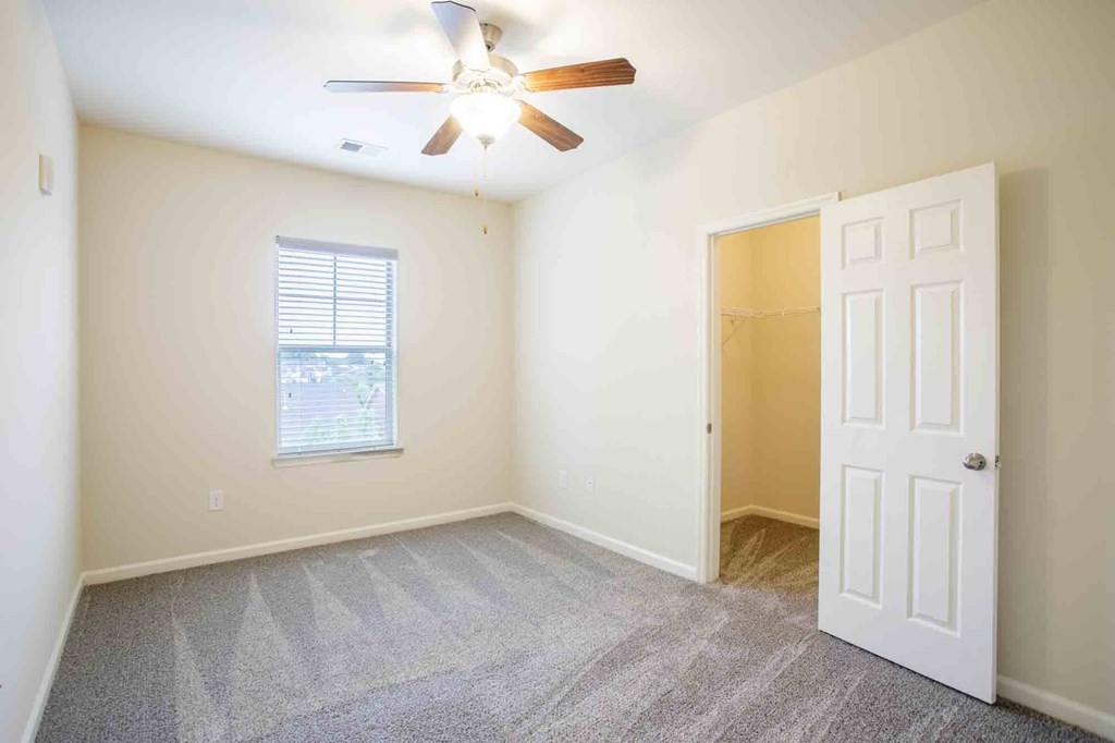 Bedroom with carpeted floors, walk-in closet, ceiling fan and a window