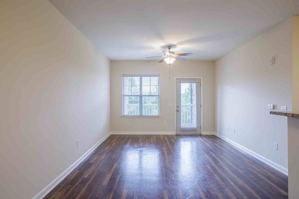 Living room with hardwood floors, a door leading to a balcony, and a ceiling fan.