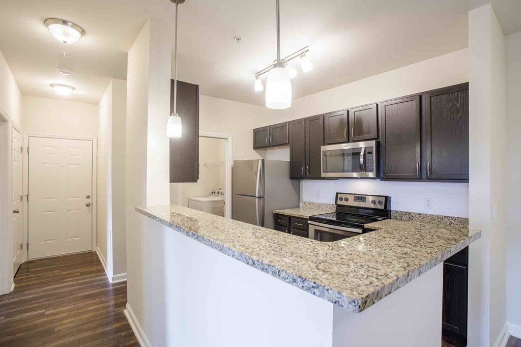 Entry way with kitchen, hardwood floors and overhead lighting.