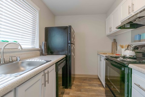 A kitchen with a black refrigerator, white cabinets, and a green stove top.