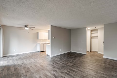 the living room and kitchen of an apartment with wood flooring and a ceiling fan