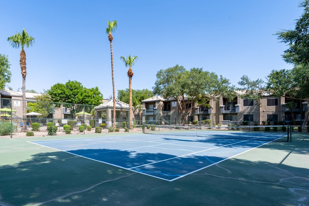 a tennis court with palm trees and apartments in the background