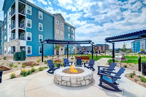A fire pit is surrounded by blue chairs in a courtyard.