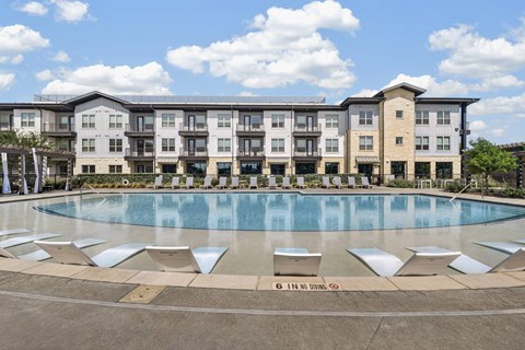A swimming pool in front of apartment buildings with a sign that says "6 in no drowning.".