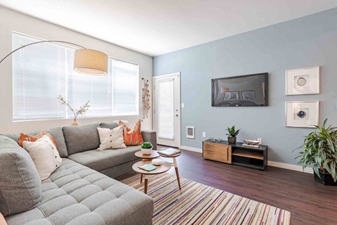 A grey couch with orange pillows sits in a living room with a wooden coffee table in front of it.