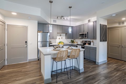 a kitchen with stainless steel appliances and a white island with two chairs