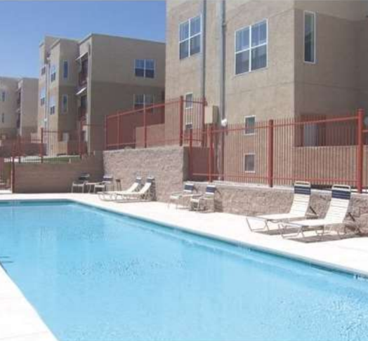 A pool surrounded by lounge chairs and a fence in front of an apartment building.