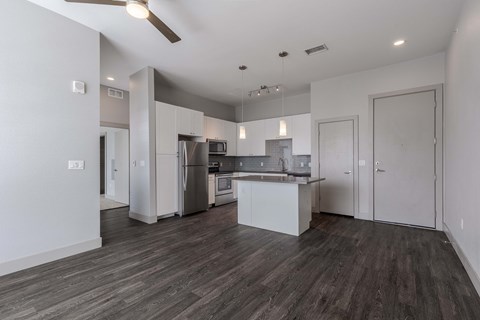 an empty living room with a kitchen with stainless steel appliances
