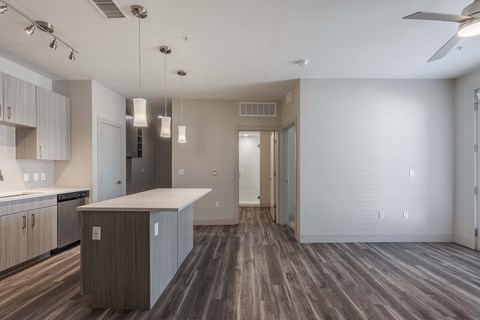 an empty living room with a kitchen and a ceiling fan