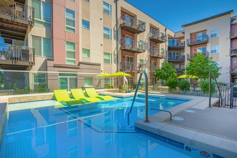 A swimming pool with yellow sun loungers in front of apartment buildings.