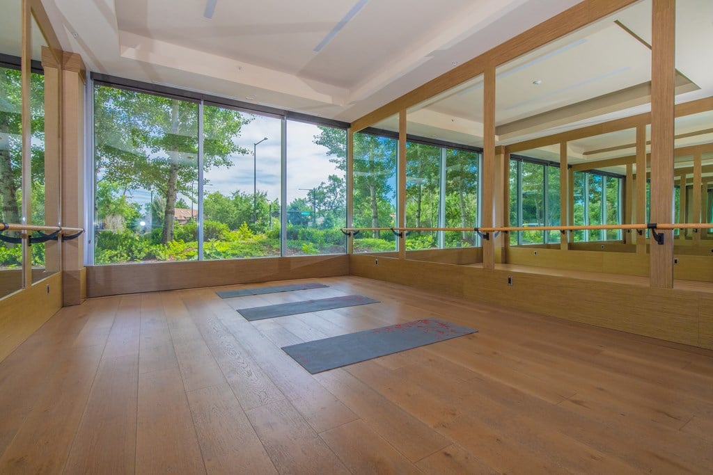 A yoga studio with wooden floors and windows overlooking a green landscape.