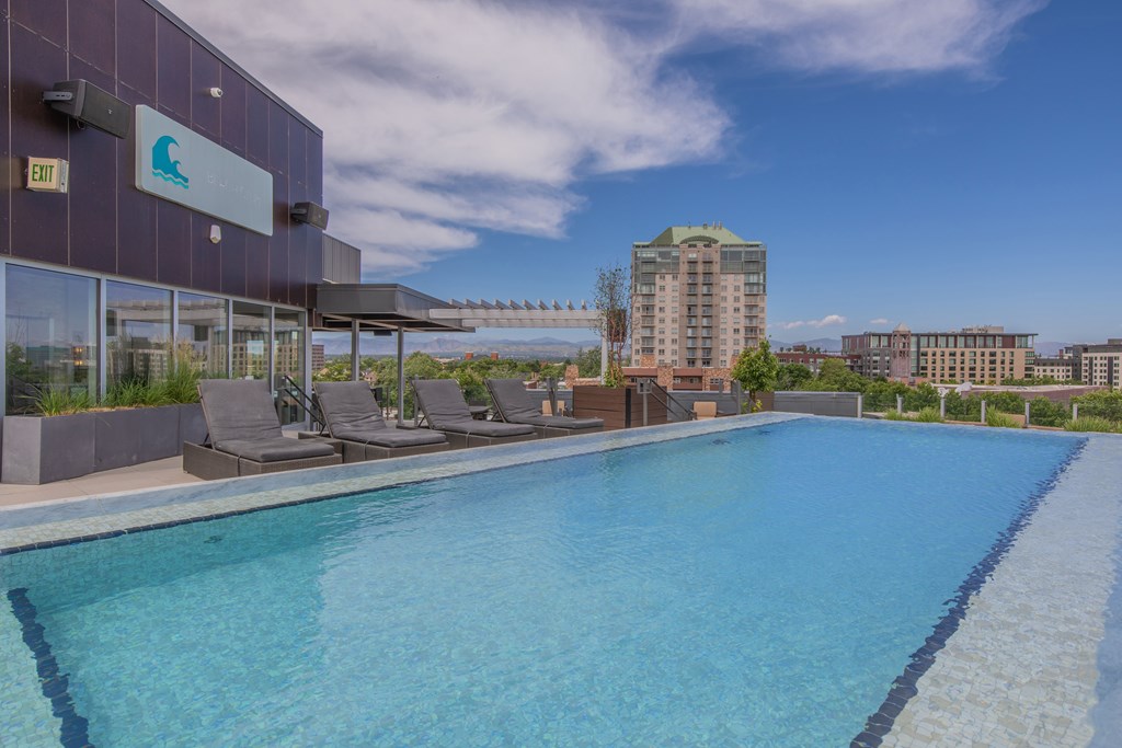A swimming pool on a rooftop with chairs and a building in the background.