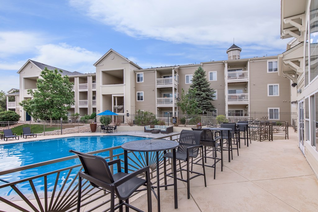 A poolside table area with chairs and a pool in front of apartment buildings.